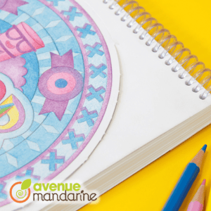 Ein teilweise farbiges Mandala ziert dieses spiralgebundene Notizbuch mit Buntstiften und dem Avenue Mandarine-Logo vor einem leuchtend gelben Hintergrund - Teil der kreativen Exacompta Clairefontaine-Kollektion.