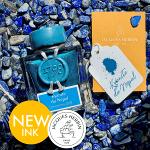 Ein Flakon der türkisblauen Tinte Kyanite du Népal von Jacques Herbin - vertrieben von Exaclair vertrieb - ist auf blauen Steinen ausgestellt, mit einer Musterkarte und einer orangefarbenen Verpackung. In den Bildecken erscheinen NEW INK und Markenlogos wie Clairefontaine, Rhodia und Quo Vadis.