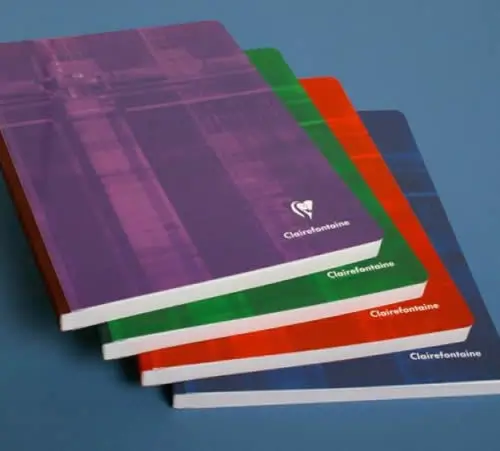 Vier Clairefontaine-Notizbücher mit violettem, grünem, rotem und blauem Einband sind leicht schief auf einer blauen Fläche gestapelt. Das vordere Notizbuch ist lila, die anderen sind darunter sichtbar.