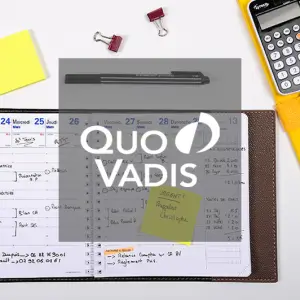Ein offener Planer mit Notizen, einem schwarzen Stift, gelben Haftnotizen, roten Büroklammern und einem Taschenrechner auf einem grauen Schreibtisch. Das Logo von Quo Vadis ist über das Bild gelegt.