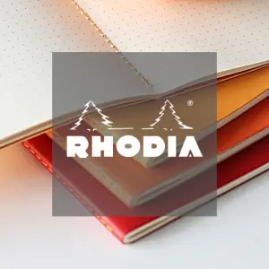 Ein Stapel aufgeschlagener Rhodia-Notizbücher mit orangefarbenem und rotem Einband, die gepunktete Seiten aufweisen. Das Rhodia-Logo mit zwei Tannenbäumen und dem Markennamen ist in der Mitte überlagert.